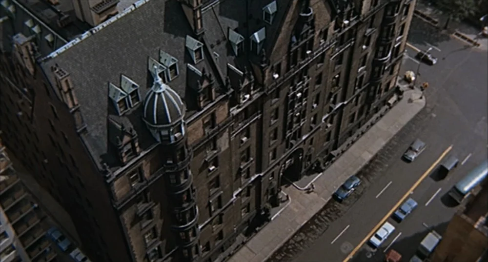 Rosemary’s Baby (1968) movie still: establishing — A historic, multi-story brick apartment building with a distinctive corner turret dominates the…