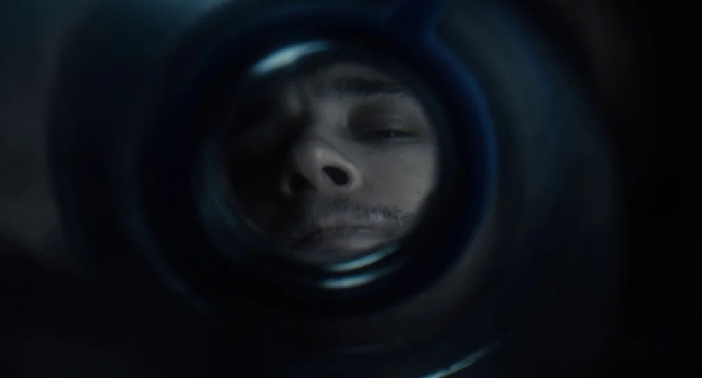 127 Hours (2010) movie still: closeup — A man's face is centered within the frame, captured through a circular dark aperture. The lighting creates a…