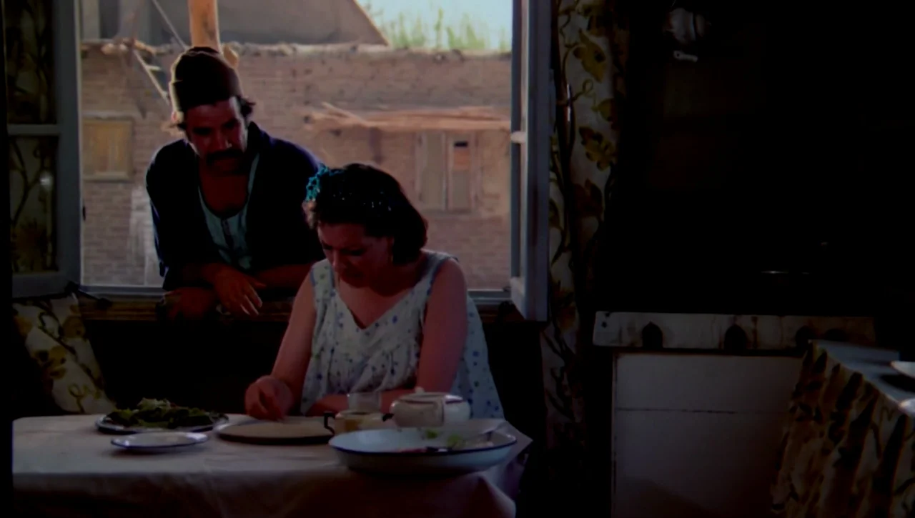 The Return of the Prodigal Son (1978) movie still: medium — A rustic interior with a small dining table sits beside a large open window. A woman…