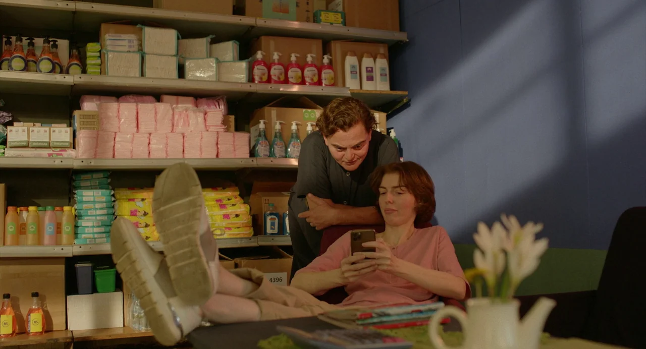 Blackbird Blackbird Blackberry (2023) movie still: medium — A cluttered stockroom with metal shelving units loaded with stacks of cleaning supplies.…