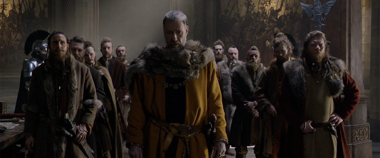 King Arthur: Legend of the Sword (2017) movie still: medium — A dimly lit stone hall features dark wood and detailed tapestry wall hangings. A…