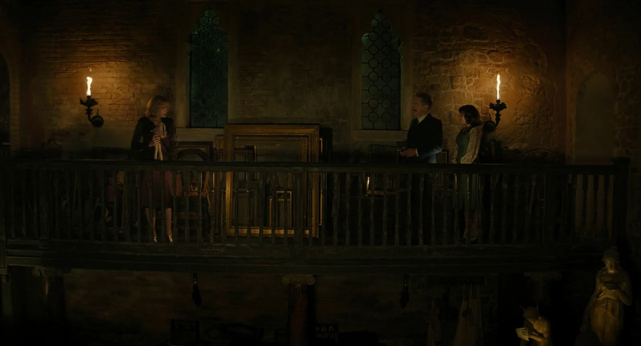 A Haunting In Venice (2023) movie still: wide — A dark stone mezzanine balcony features a wooden railing and ornate, narrow leaded windows. Three…