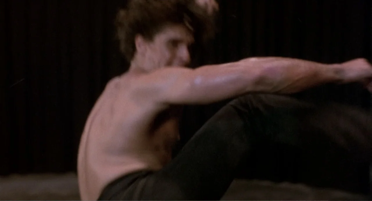 American Ninja 3: Blood Hunt (1989) movie still: medium — A dark indoor space with a plain black curtain serving as the backdrop. A shirtless man…