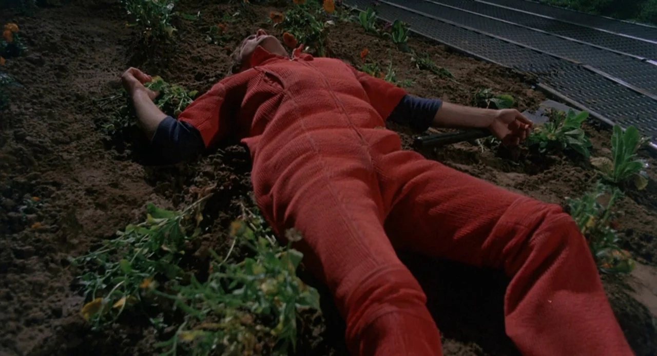 Silent Running (1972) movie still: fullbody — A man in a red jumpsuit lies flat on his back in a flowerbed. He rests on dark soil alongside young…