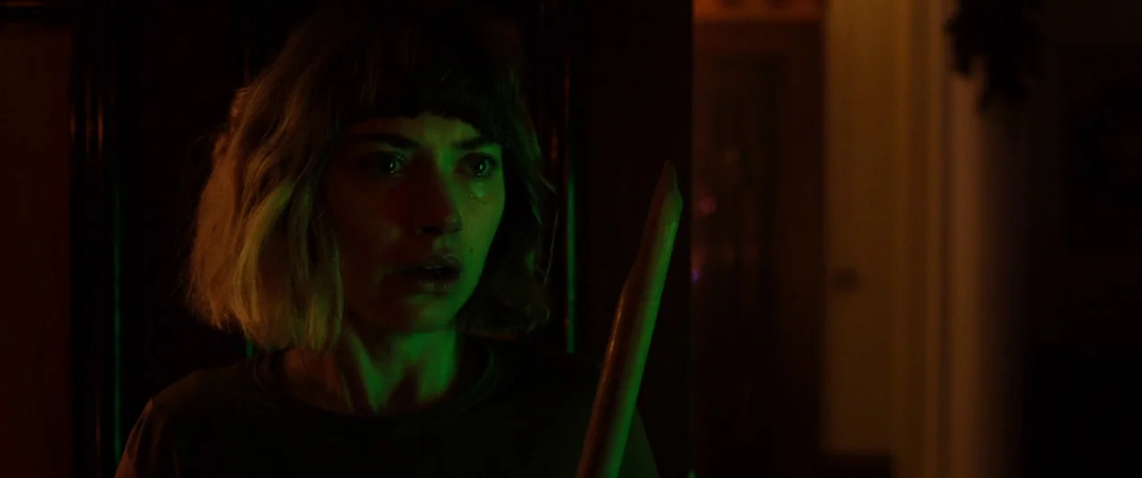Black Christmas (2006) movie still: closeup — A dark, dimly lit corridor with indistinct background walls. A woman holds a wooden stake, illuminated…
