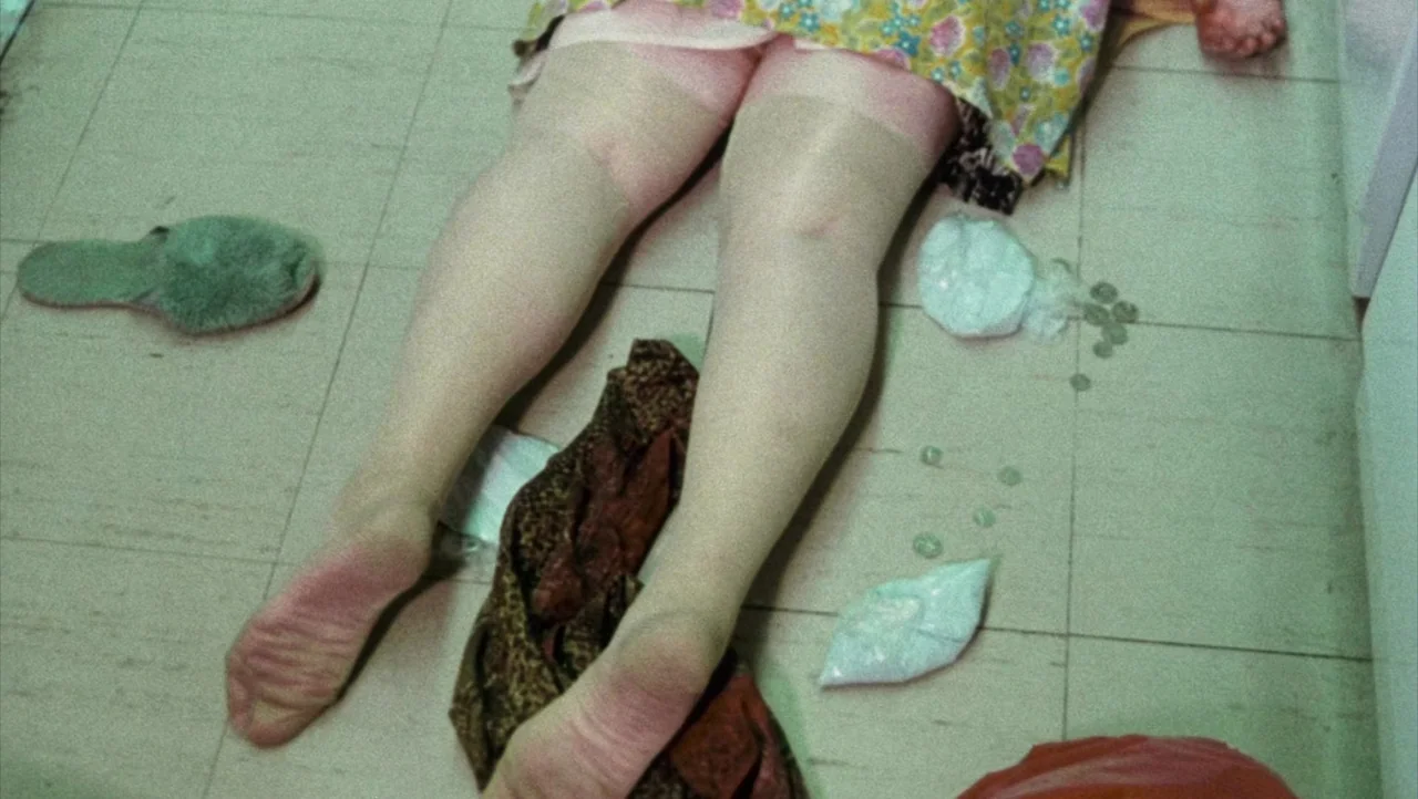 Shivers (1975) movie still: fullbody — A light-tiled bathroom floor is cluttered with small plastic bags filled with white powder. A pair of legs…