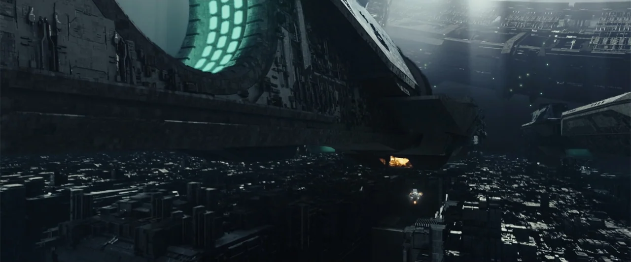 Moonfall (2022) movie still: establishing — A gargantuan mechanical vessel drifts above a dense, dark metropolis of metallic, boxy buildings. Small…