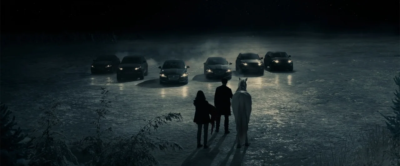 Winter's Tale (2014) movie still: wide — A dark, snow-covered frozen lake at night contains a line of luxury vehicles. A man, a woman, and a white…
