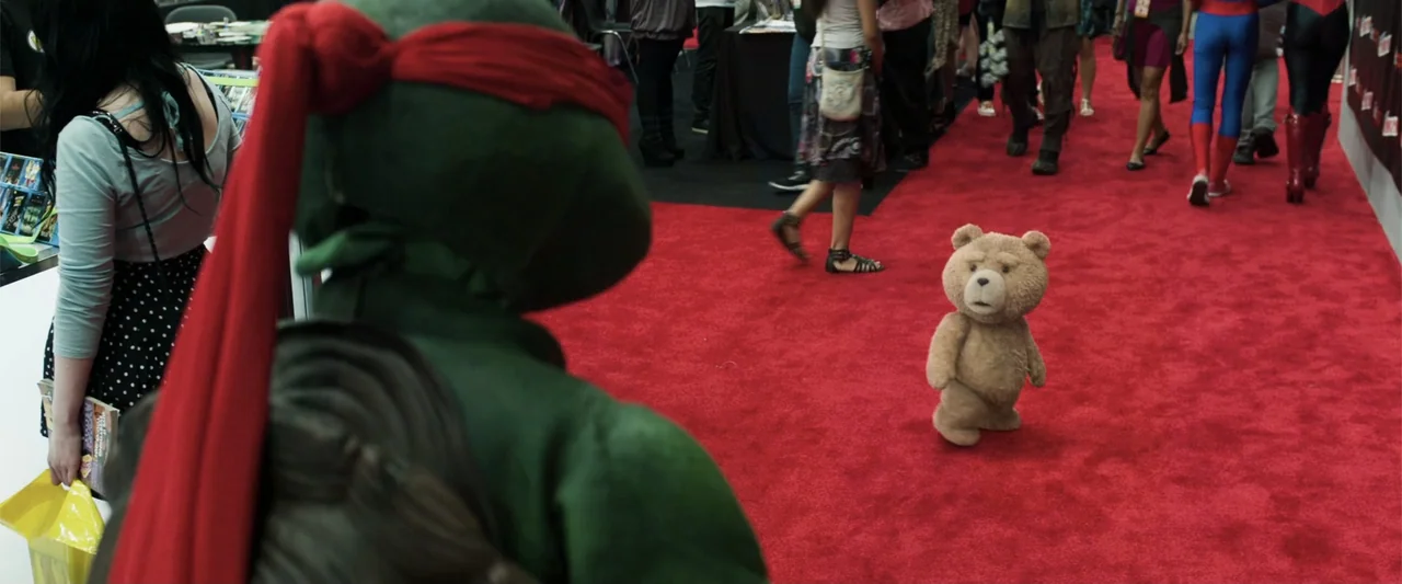 Ted 2 (2015) movie still: medium — A bright convention hall interior features a vibrant red carpet stretching across the floor. A person in a green…