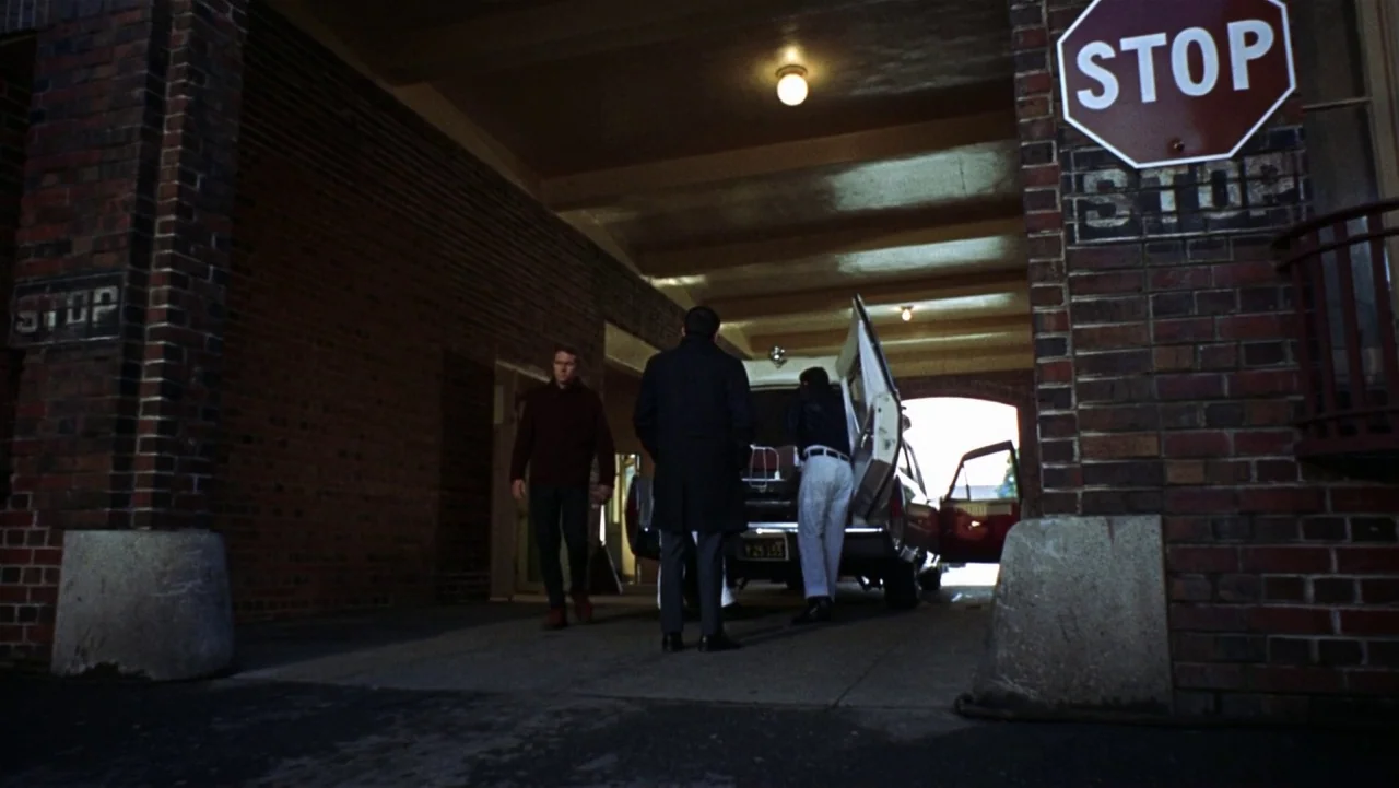Bullitt (1968) movie still: wide — A brick-walled structure with a covered driveway serves as an ambulance bay. Three men stand near an ambulance…