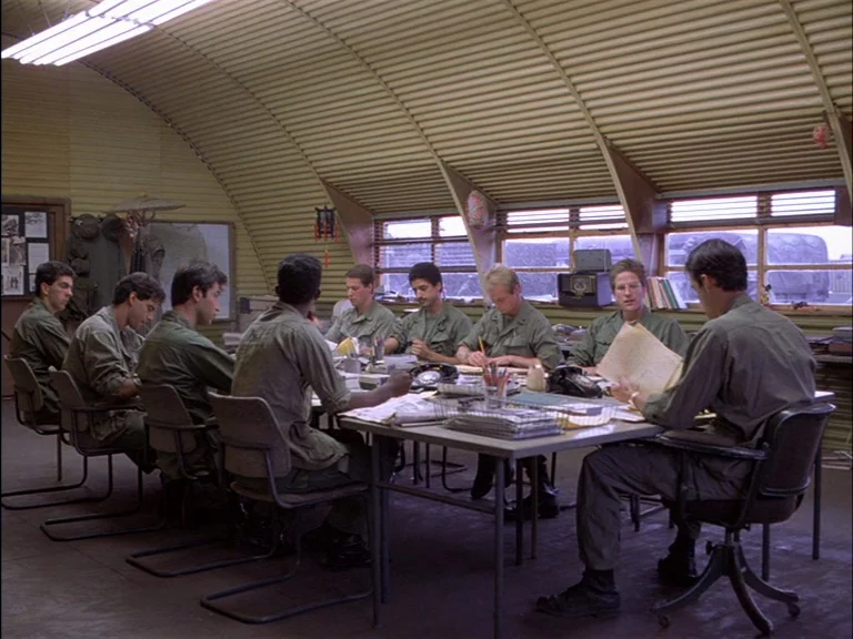 Full Metal Jacket (1987) movie still: wide — A Quonset hut interior features a long table surrounded by men in military uniforms. The soldiers sit…