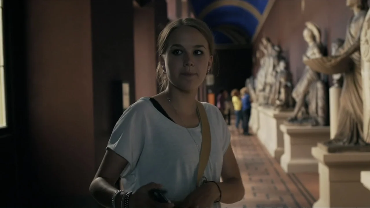 Copenhagen (2002) movie still: medium — A museum hall features a row of classical marble statues on pedestals lining one side. A young woman walks…