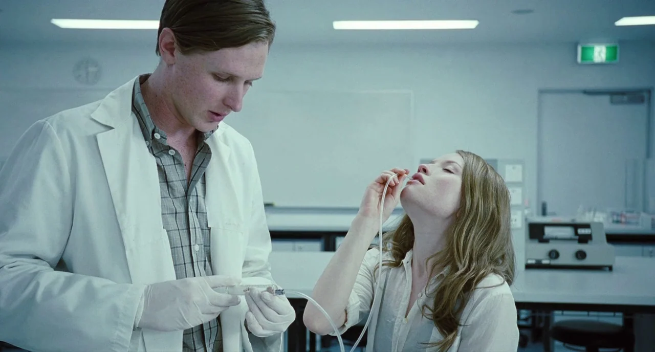 Sleeping Beauty (2011) movie still: medium — A sterile medical laboratory with white walls and a large, empty whiteboard. A man holding a syringe…