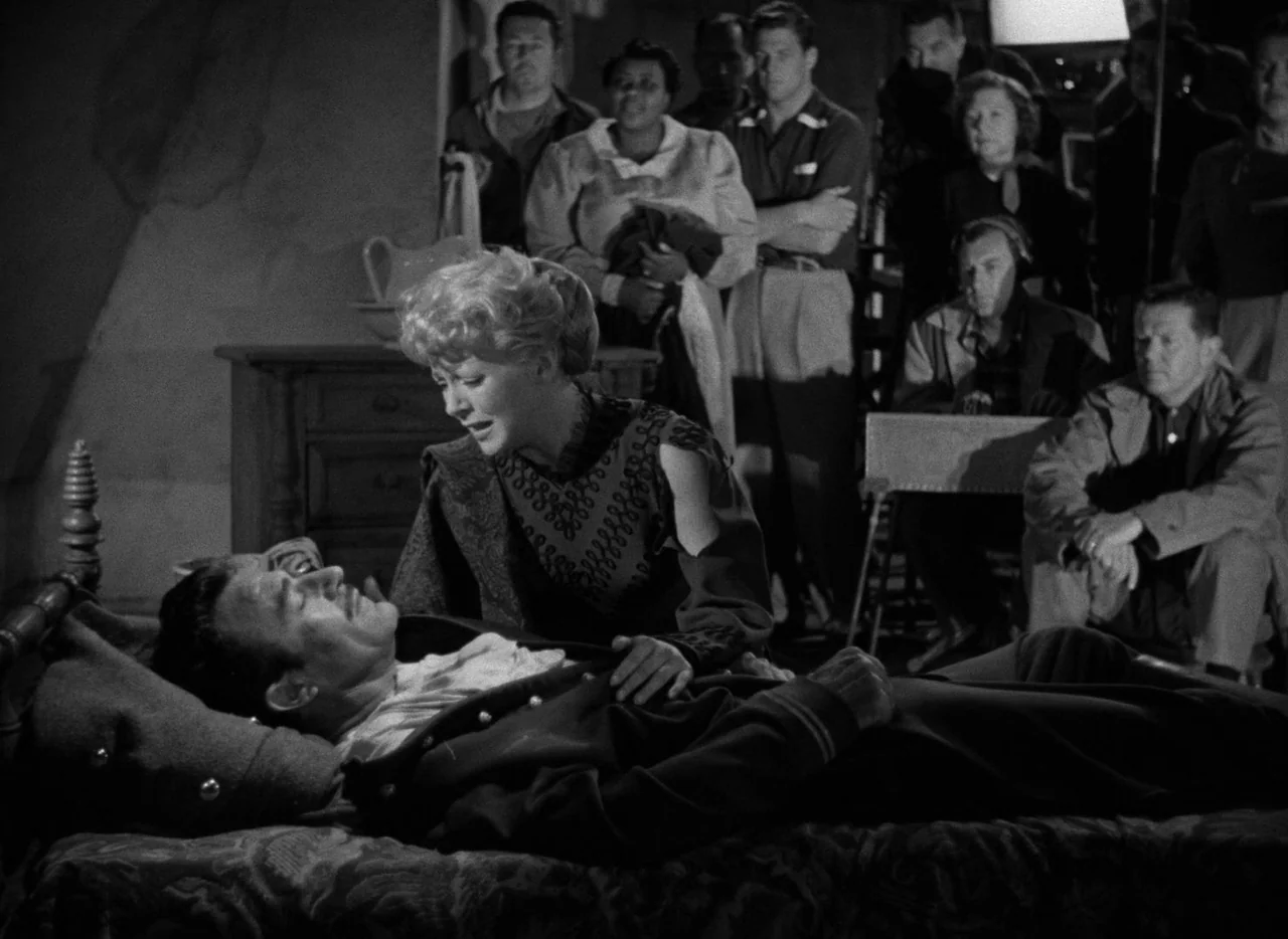 The Bad and the Beautiful (1952) movie still: medium — A dimly lit room contains a bed where a woman attends to a man. Other individuals observe the…