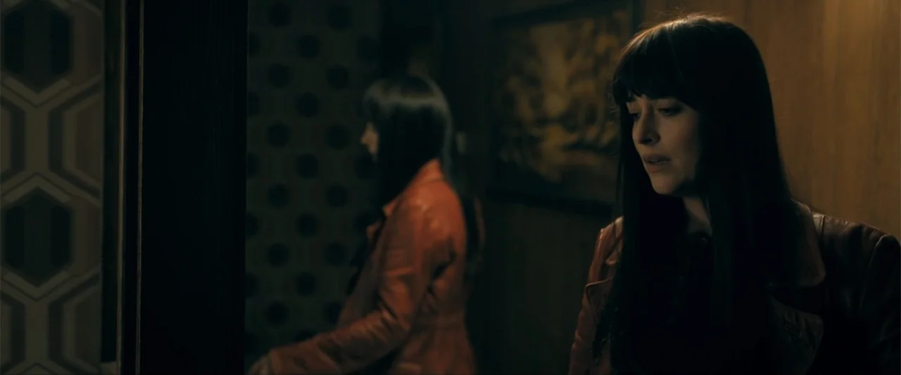 Madame Web (2024) movie still: medium — A dimly lit interior space with dark patterned wallpaper and wood paneling. A woman in the foreground looks…
