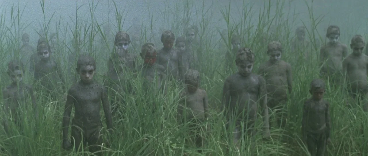 Vinyan (2008) movie still: wide — A dense field of tall green grass is filled with many children standing together. The children have mud-covered…
