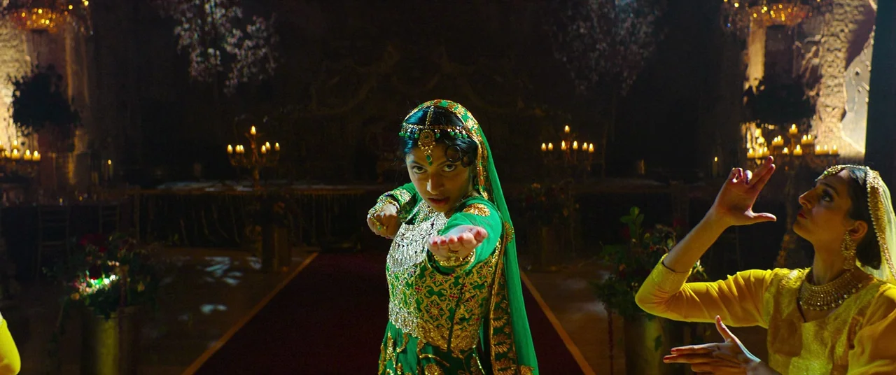 Polite Society (2023) movie still: medium — A dimly lit banquet hall features floral arrangements and many lit candles on tables. Two dancers in…