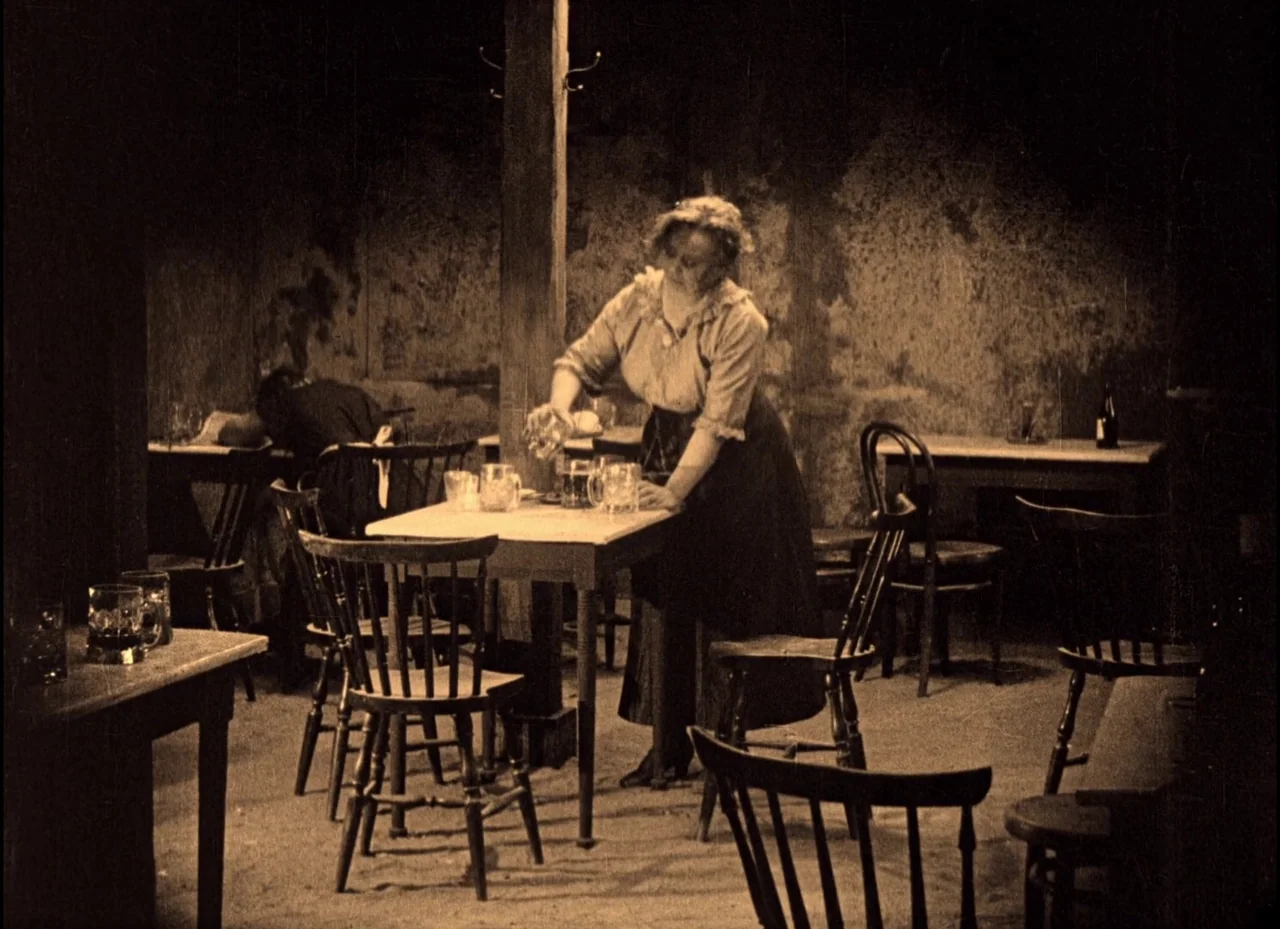 The Phantom Carriage (1921) movie still: fullbody — A dimly lit, rustic tavern features weathered wooden walls and several simple dining tables. A…