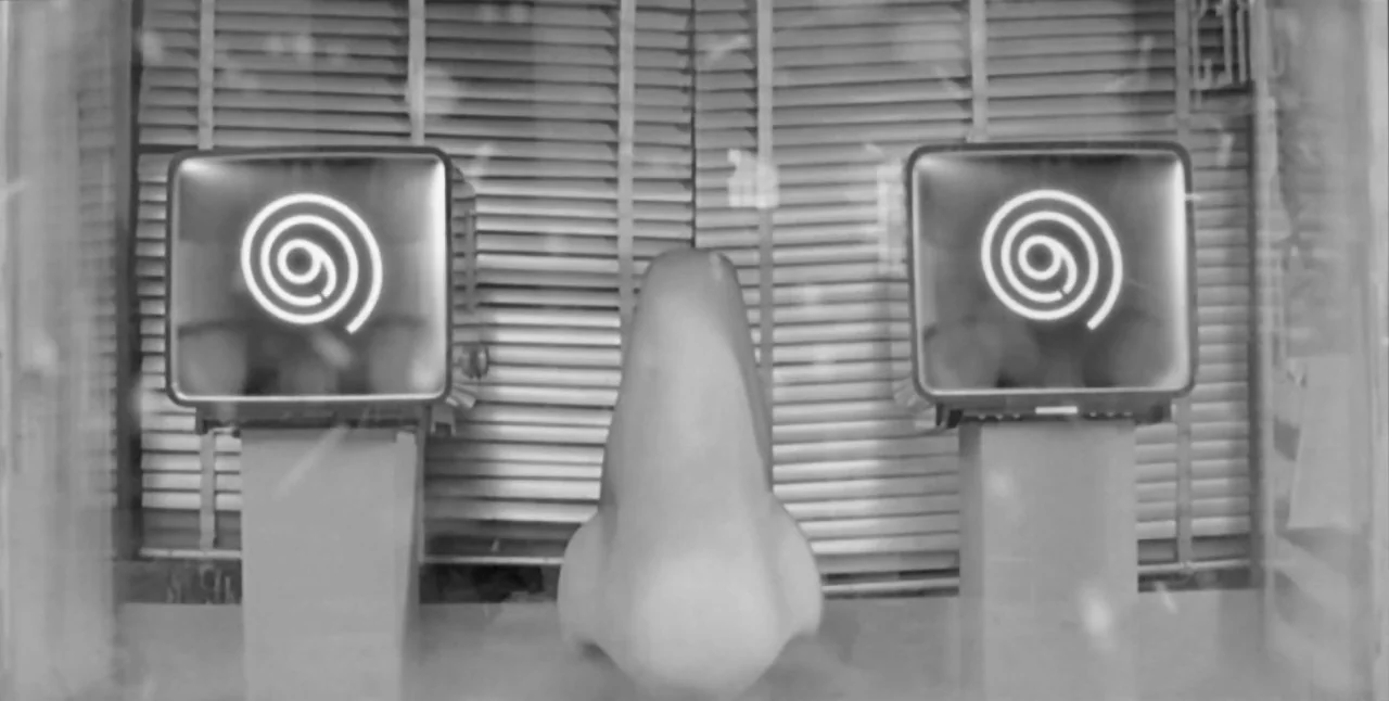 The Aerial (2007) movie still: closeup — A store window display features a large nose sculpture flanked by two television sets. The television…