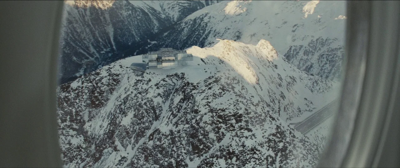 Spectre (2015) movie still: establishing — A high-altitude mountain peak is covered in snow with a glass structure at the top. The view is framed…