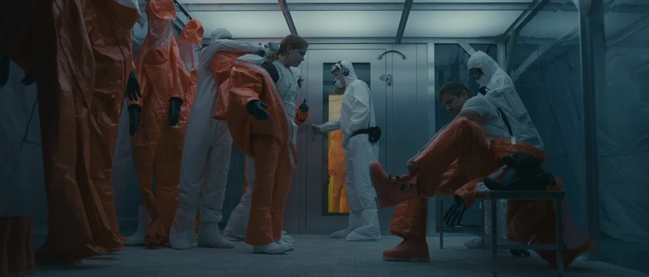 Arrival (2016) movie still: wide — A sterile decontamination room features metallic walls, glass partitions, and rows of hanging safety suits. A…