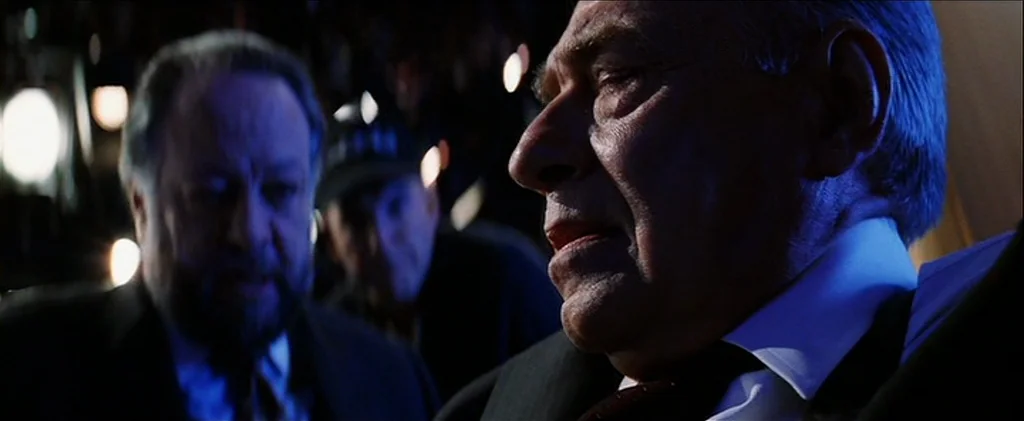 Magnolia (1999) movie still: closeup — A dark airplane cabin features two men seated in business or first class rows. The man in the foreground is…