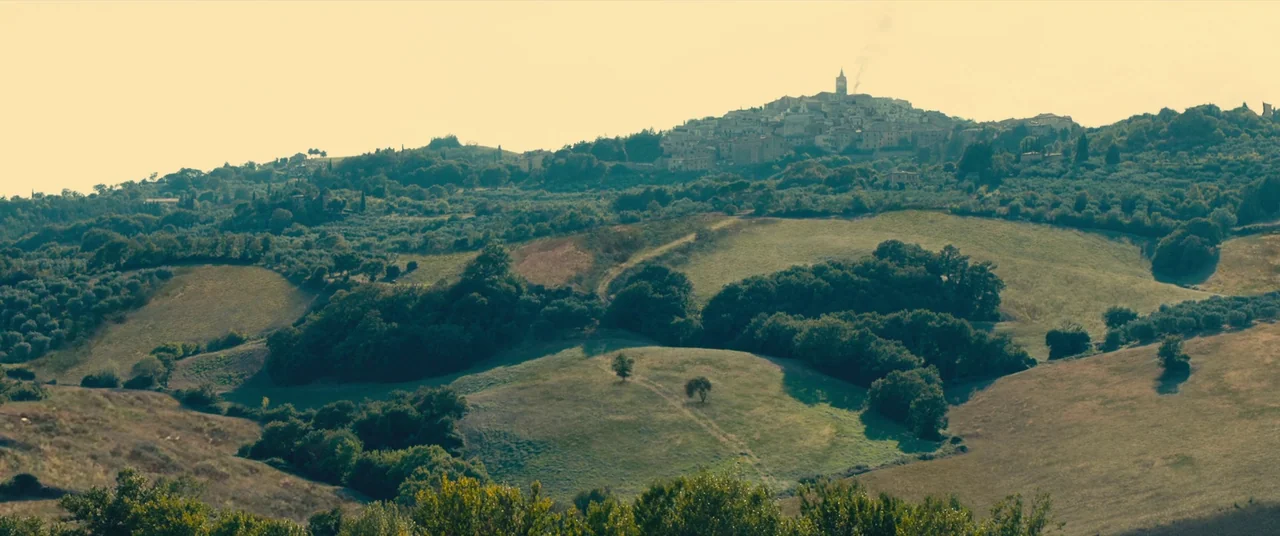 Benedetta (2021) movie still: establishing — A view of rolling hills in an Italian landscape with scattered trees and vegetation. A small town sits…