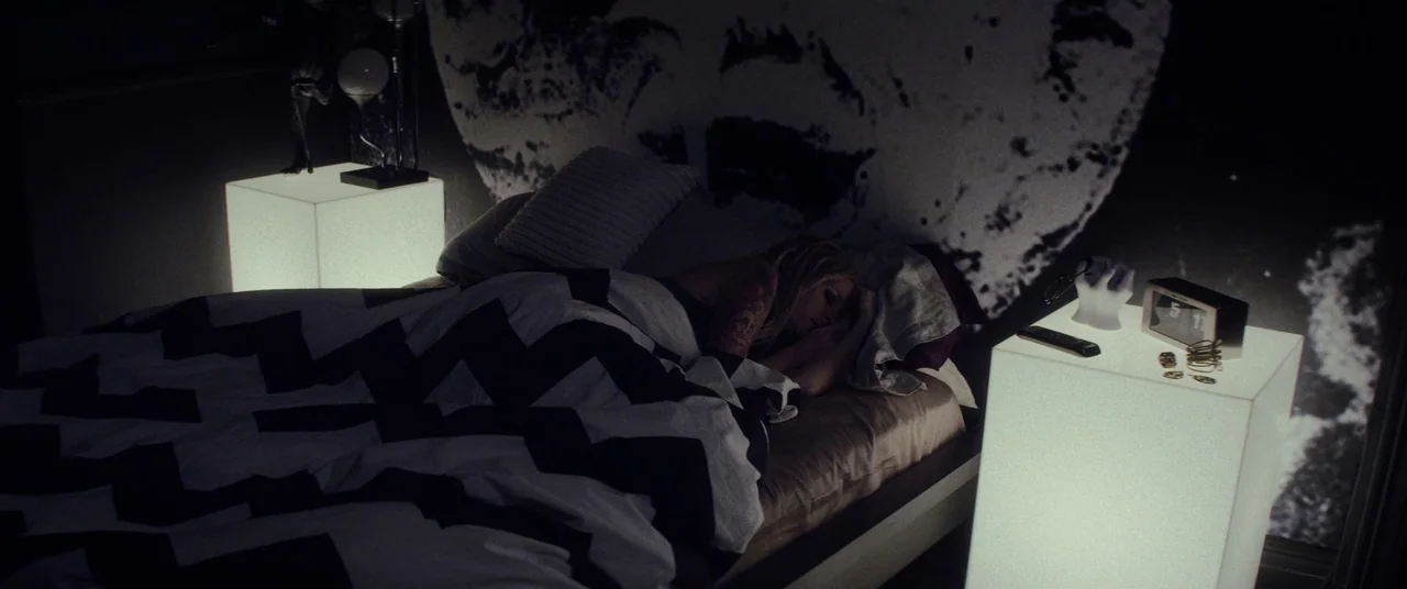 Lords Of Salem (2013) movie still: medium — A dark bedroom features two glowing cubic nightstands and a large graphic wall print. A woman sleeps on…