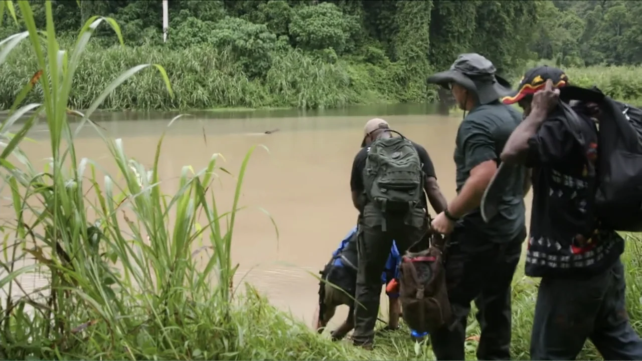 Finding Amelia (2024) movie still: medium — A group of three people stand at the edge of a muddy riverbank. The individuals look towards the water…