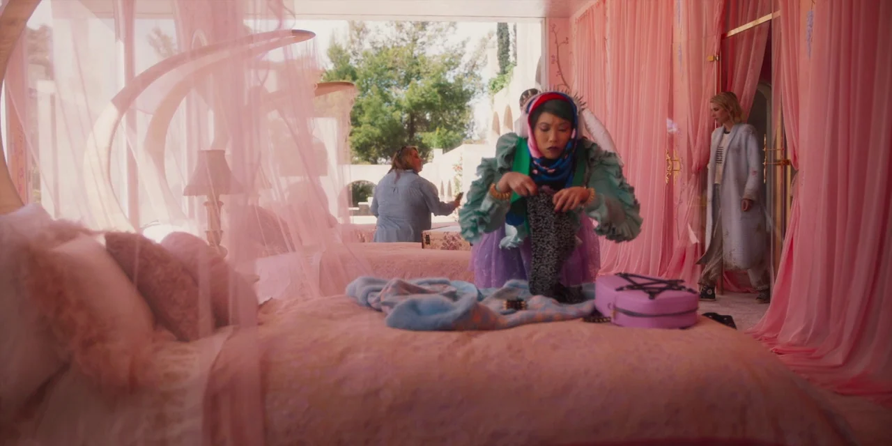 Paradise Hills (2019) movie still: wide — A pink-themed hotel suite features draped curtains and twin beds. One person stands in the foreground…