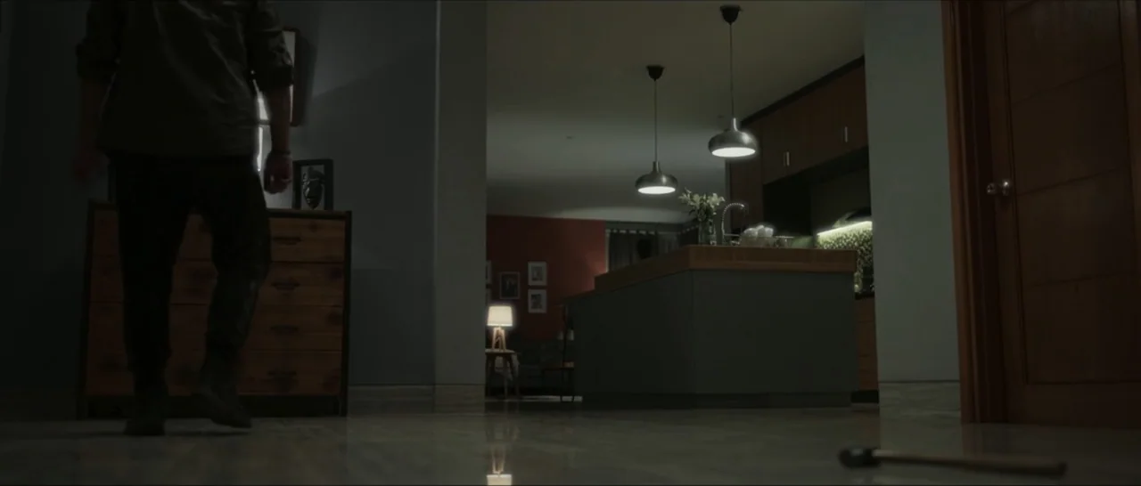 Innocent Vengeance (2023) movie still: fullbody — An dimly lit modern home interior features an open plan area with a kitchen island. A lone male…