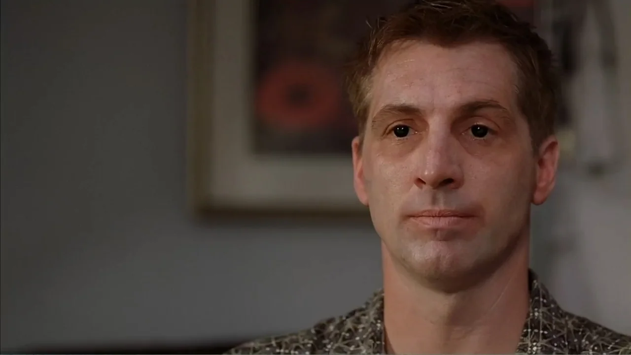 Day of the Dead 2: Contagium (2005) movie still: closeup — An interior space with a blurred picture frame on the wall behind the subject. A man in a…