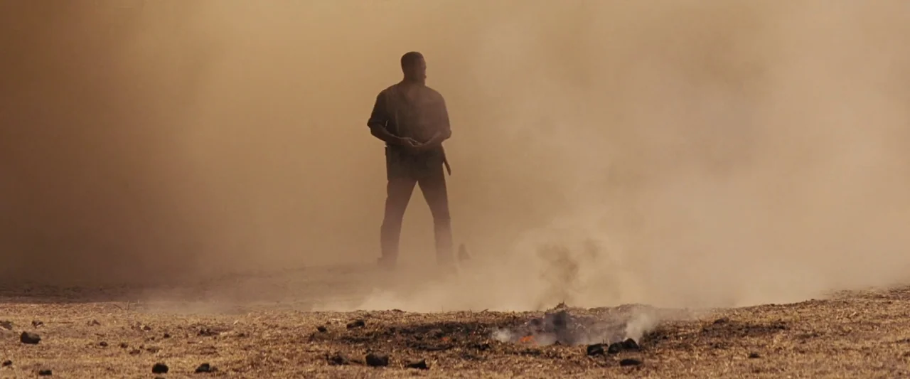 Django Unchained (2012) movie still: fullbody — A man stands in a vast, dry field filled with billowing clouds of dust. He stares toward the…