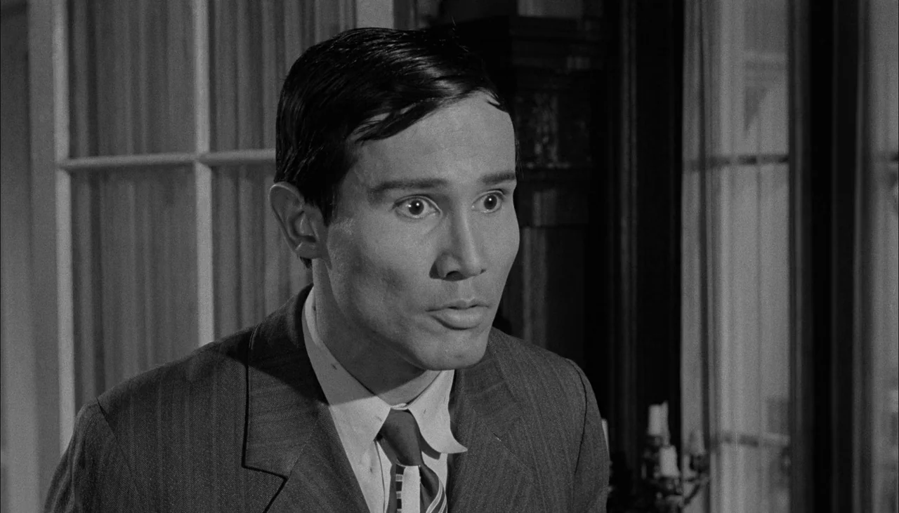 The Manchurian Candidate (1962) movie still: medium — A dimly lit indoor study features dark wood paneling and window frames in the background. A…