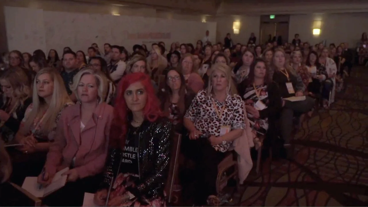 The Rise and Fall of Lularoe (2021) movie still: medium — A crowded interior conference hall filled with rows of seated attendees facing forward.…