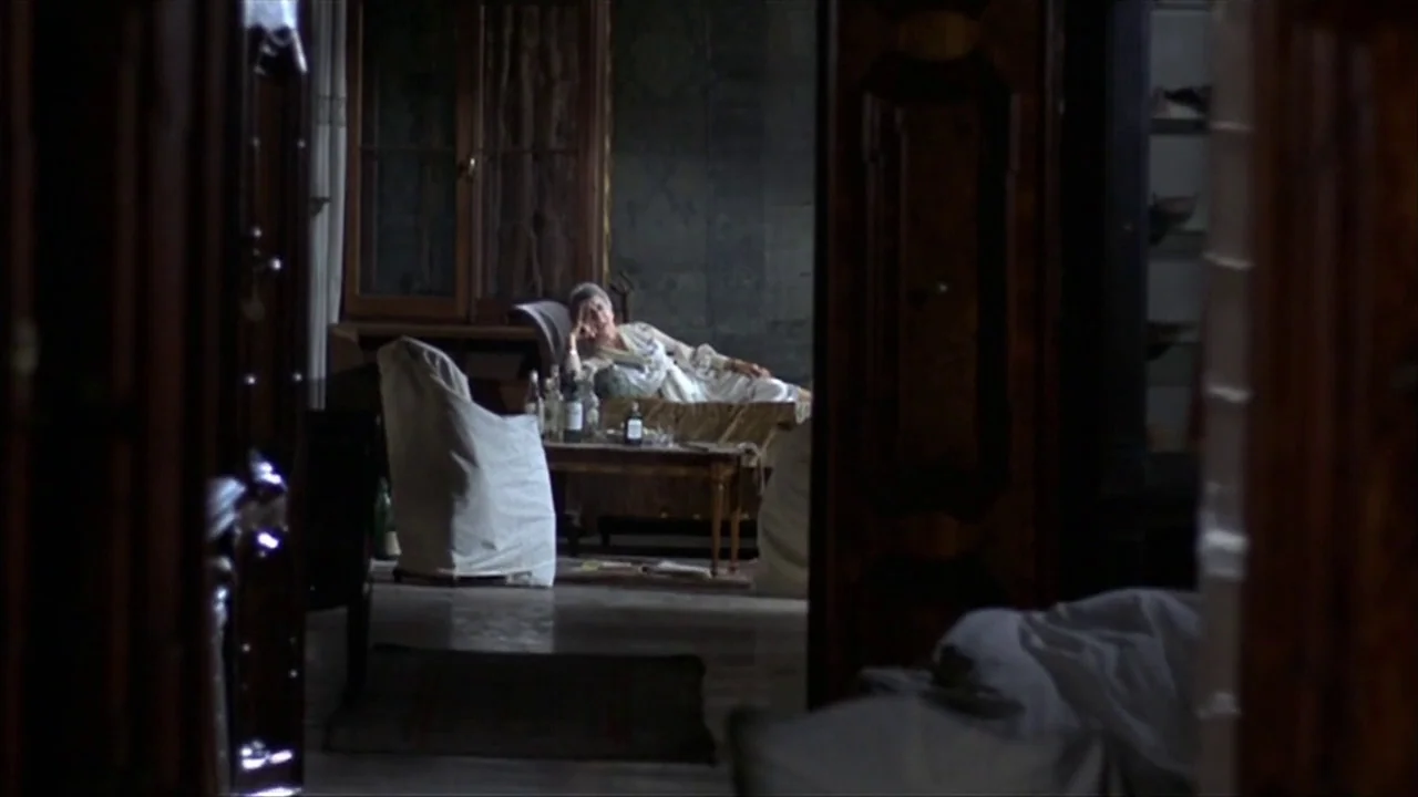 A Quiet Place In The Country (1968) movie still: wide — An interior space features draped furniture and wooden cabinets in a dimly lit room. A woman…