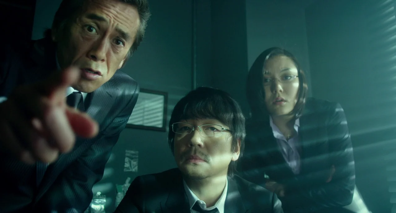 Helter Skelter (2012) movie still: medium — A dark office environment features horizontal light streaks from window blinds covering the room. Three…