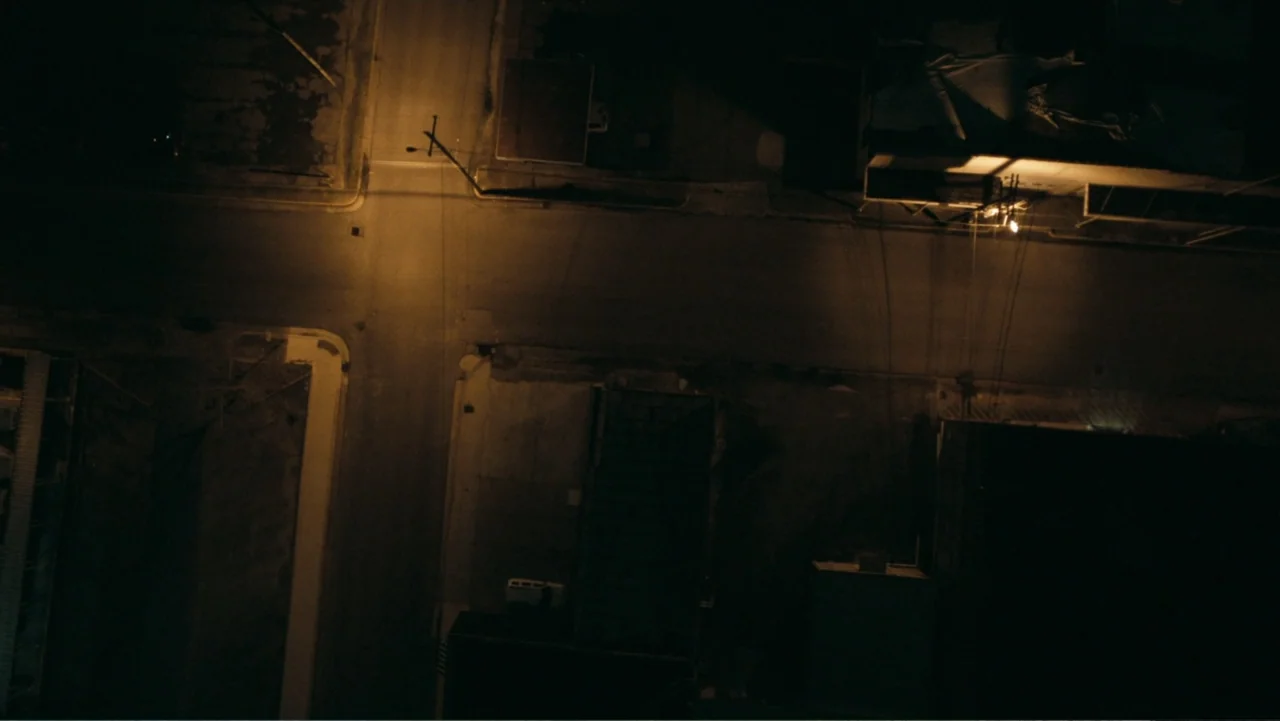 Alabama Snake (2020) movie still: establishing — An aerial view of a dark city street intersection at night. Yellow streetlights create sharp…