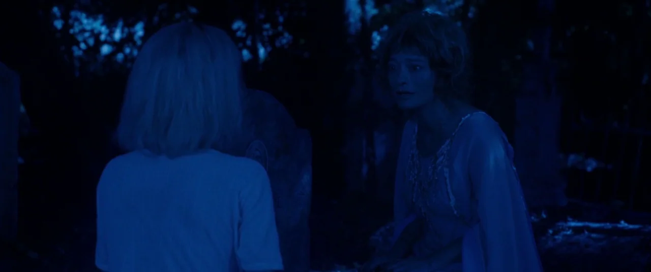 Knife+Heart (2018) movie still: medium — A night scene in a dark, outdoor cemetery with tombstones partially obscured by shadows. A woman sits on…