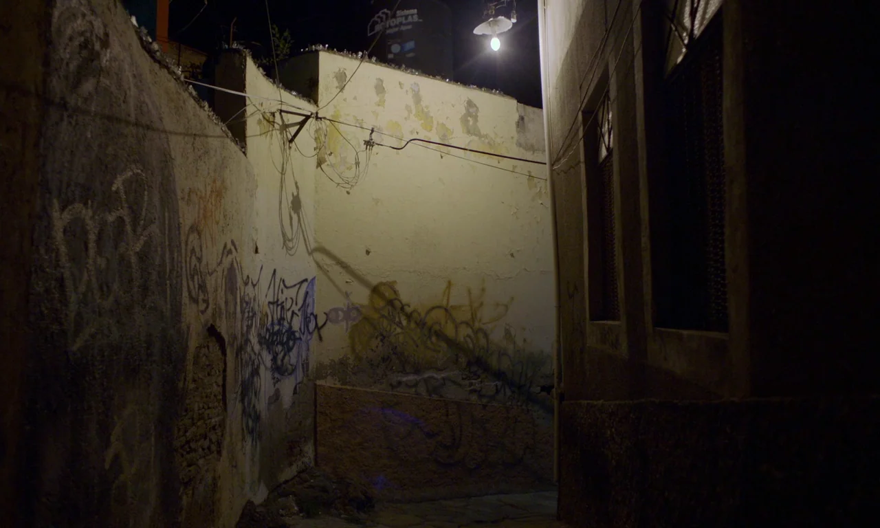 The Untamed (2016) movie still: establishing — A narrow alleyway with textured stucco walls covered in weathered graffiti and peeling paint. A…