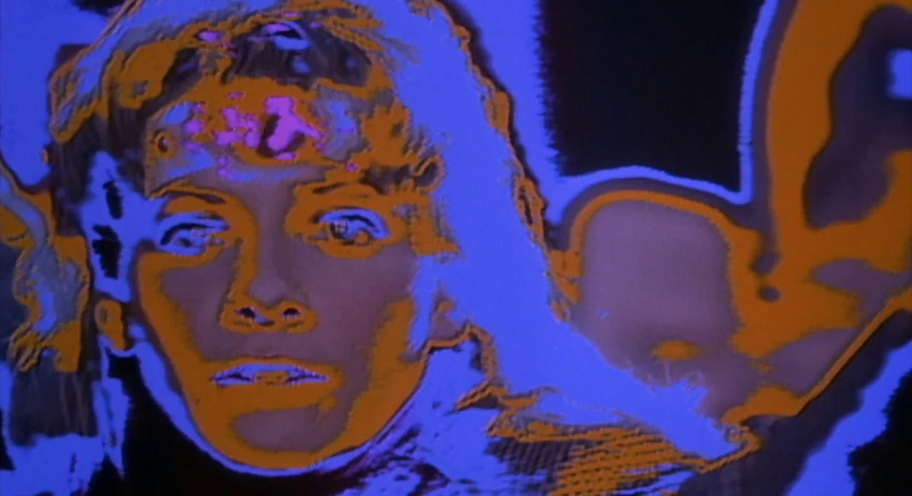 From Beyond (1986) movie still: closeup — A close-up view of a person's face treated with high-contrast color posterization effects. The image…
