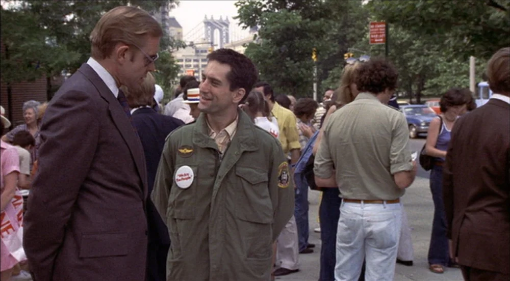 Taxi Driver (1976) movie still: medium — A bustling public sidewalk in New York City with numerous pedestrians moving past. Two men stand in the…