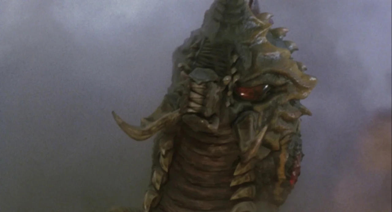 Godzilla and Mothra: The Battle for Earth (1992) movie still: closeup — A textured alien creature head fills the frame against a backdrop of thick…