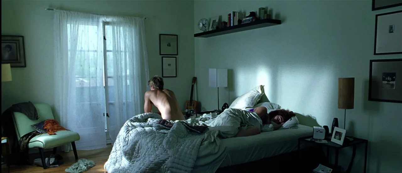 The Mexican (2001) movie still: wide — A light green room contains a bed with a white quilt and bedside furniture. A shirtless man sits on the edge…
