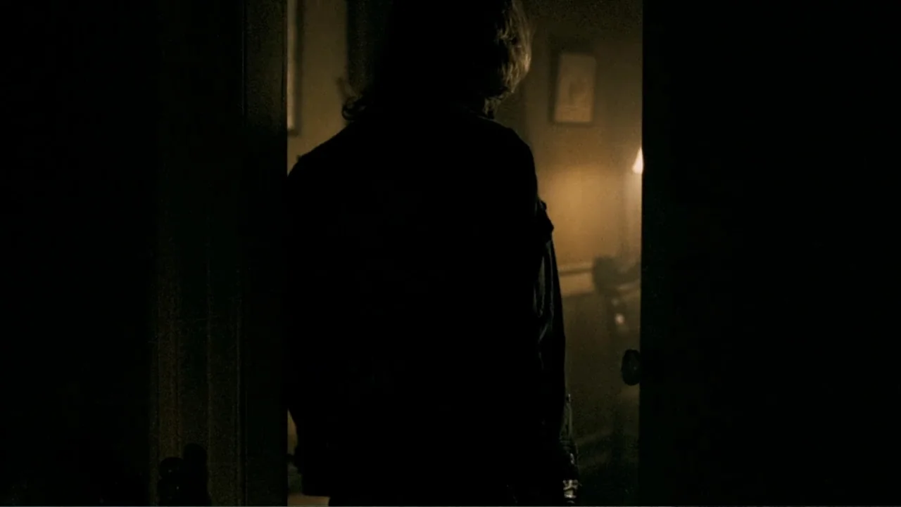 The Texas Chainsaw Massacre: The Beginning (2006) movie still: medium — A dark, silhouetted figure stands in the threshold of a doorway. Beyond the…