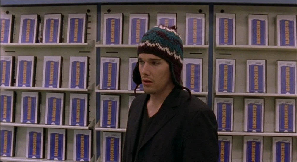 Hamlet (2000) movie still: medium — A man stands before rows of uniform video rental cases inside a commercial store. The background is composed of…