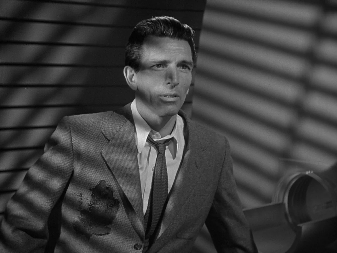 The Day the Earth Stood Still (1951) movie still: medium — A man stands in a room with light filtering through horizontal window blinds. He wears a…