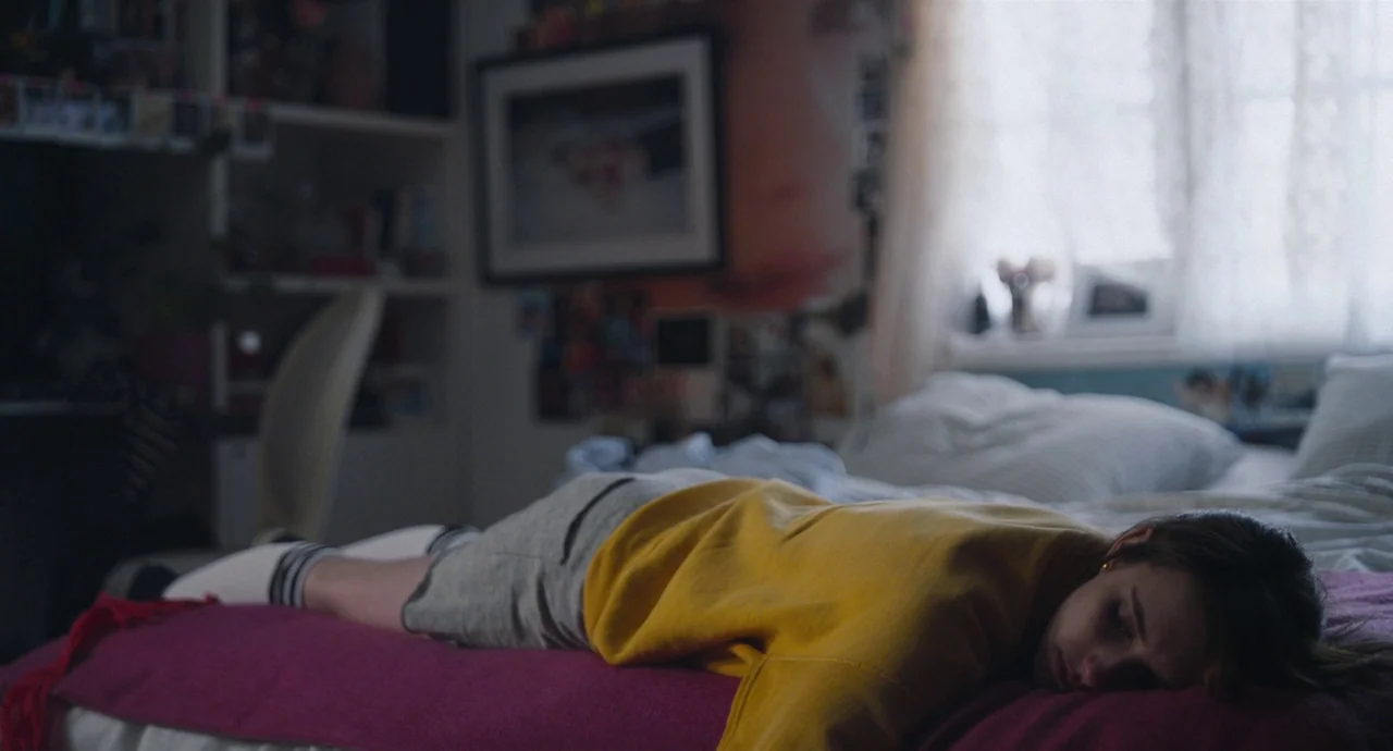 Palo Alto (2013) movie still: medium — A cluttered teenager's room with posters on the walls and a window with curtains. A girl rests on the magenta…