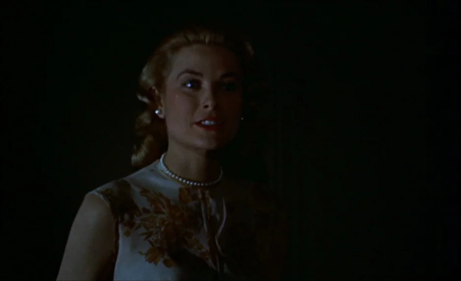 Rear Window (1954) movie still: medium — A dark, minimally lit room with no visible environmental details beyond the subject. A woman stands in the…