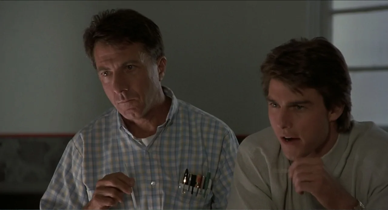 Rain Man (1988) movie still: medium — An interior space features two men side by side in a dimly lit room. They watch something intently while…
